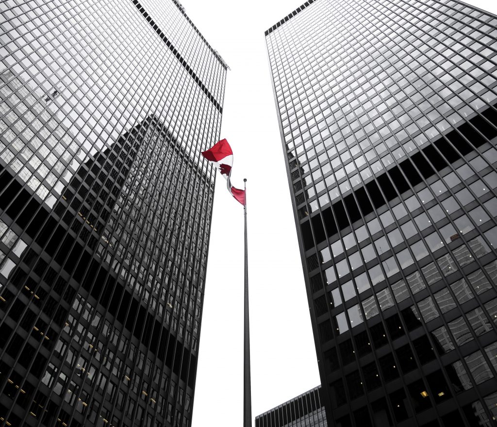 Photographie à faible angle des tours de grande hauteur et le drapeau canadien flottant au milieu Photographie à faible angle des tours de grande hauteur et le drapeau canadien flottant au milieu